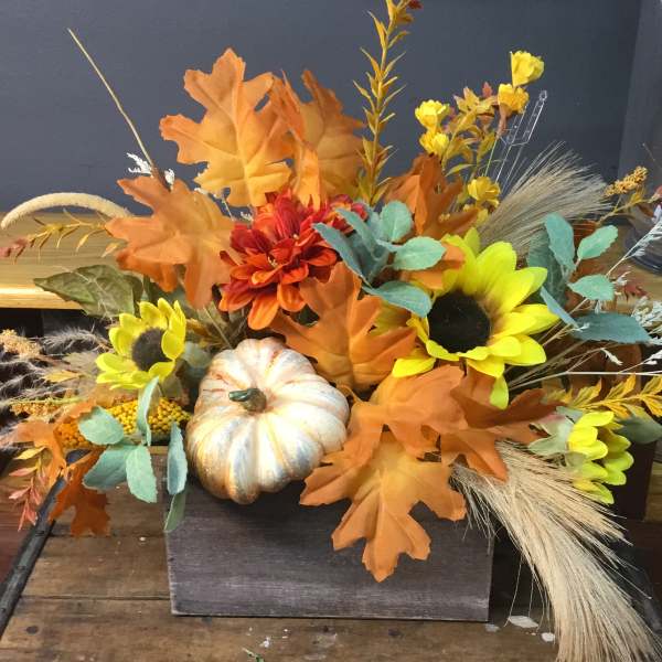 Autumn floral arrangement with sunflowers, orange blooms, and a decorative pumpkin
