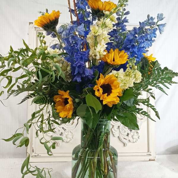 Tall bouquet of sunflowers and blue delphinium in a glass vase