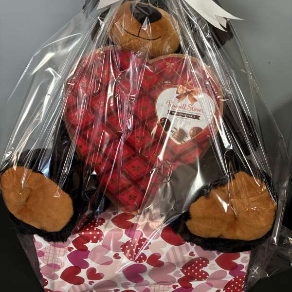 Gift basket with a teddy bear and heart-shaped chocolate box wrapped in cellophane