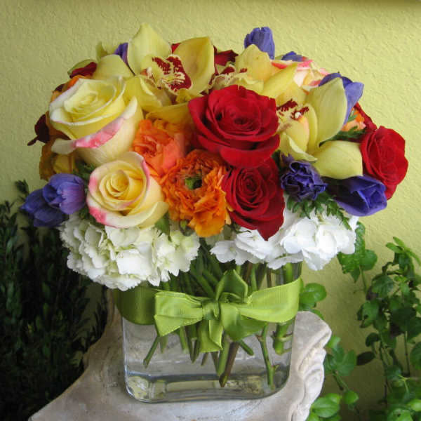 Colorful bouquet of roses and orchids in a glass vase with a green ribbon