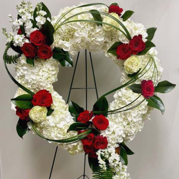 Heart-shaped floral wreath with red roses and white hydrangeas on a stand