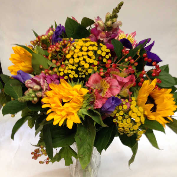 Mixed bouquet of sunflowers, pink blooms, and yellow filler flowers in a glass vase