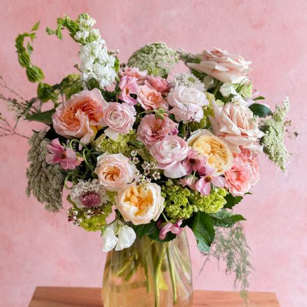 Pastel bouquet of roses, ranunculus, and mixed blooms in a glass vase
