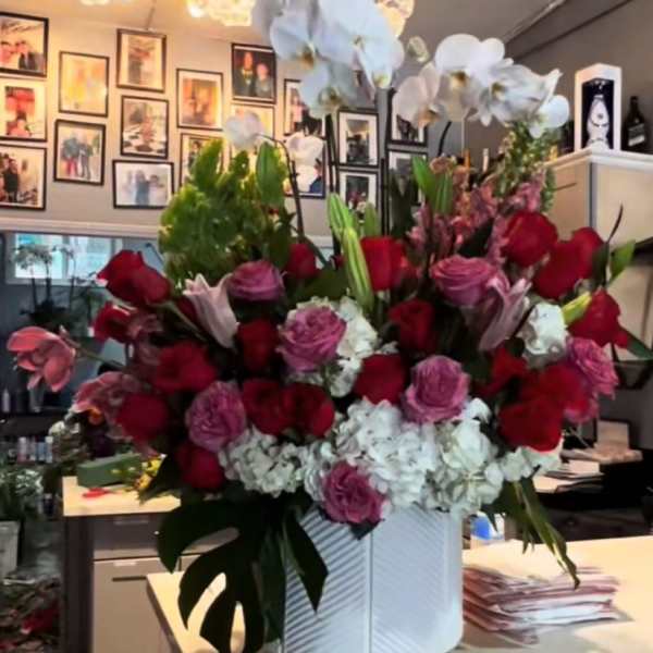 Large floral arrangement with red and pink roses, white hydrangeas, and white orchids in a white vase.