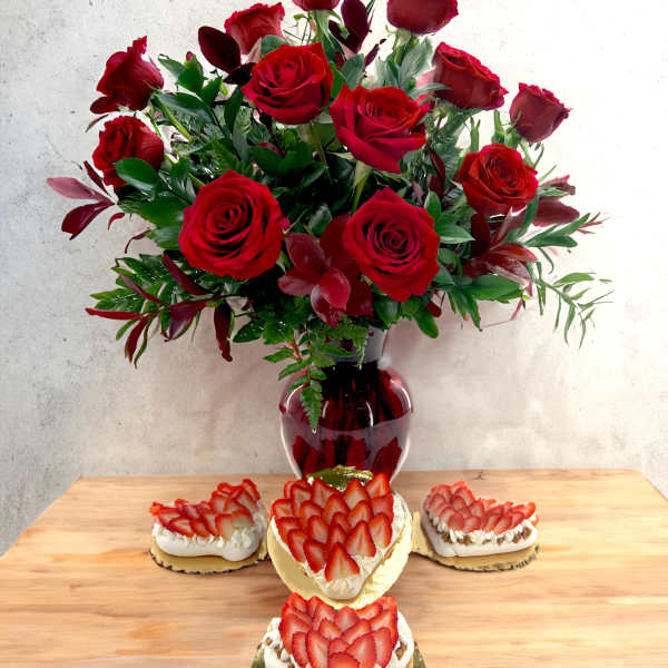Red rose bouquet in a red vase with strawberry-topped desserts on a table