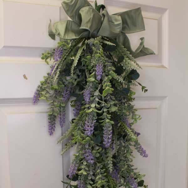 Hanging greenery swag with purple flowers and a large ribbon bow
