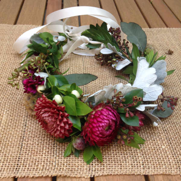 Floral wreath with pink blooms and white ribbon on a burlap mat