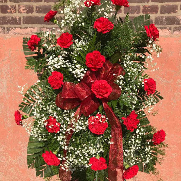 Standing spray of red carnations with white baby's breath and a red ribbon