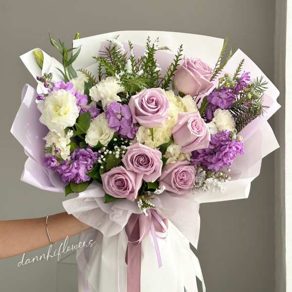 Hand-tied bouquet of lavender roses and purple-white blooms wrapped in pastel paper
