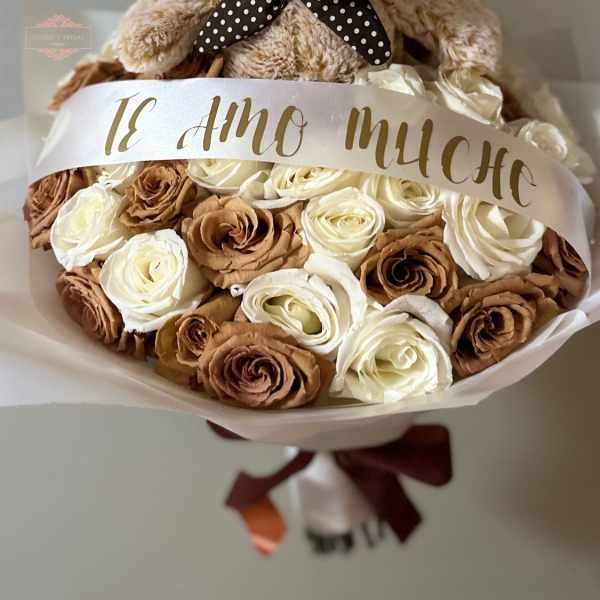 Teddy bear atop a bouquet of cream and brown roses with a ribbon