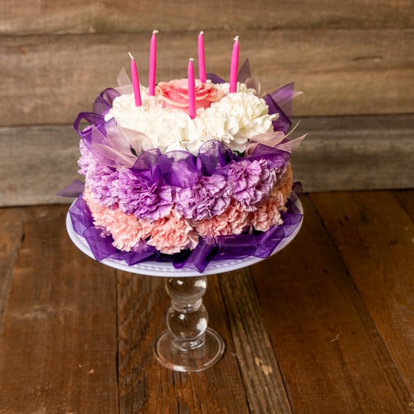 Round floral cake with pink candles on a glass pedestal