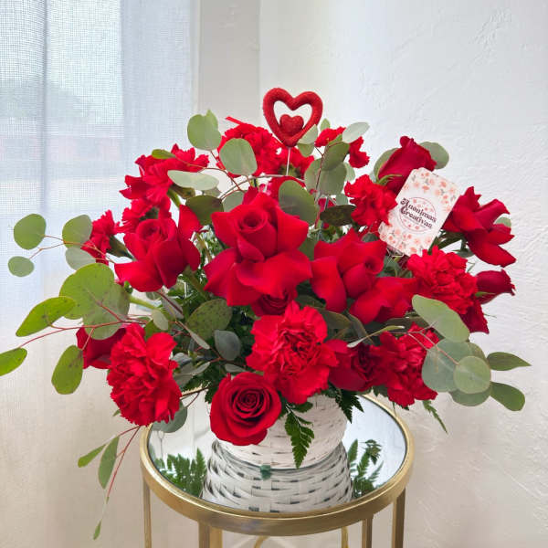 Red roses and carnations in a white woven vase with a heart pick