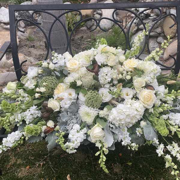 White floral arrangement with roses and mixed blooms on a black metal bench