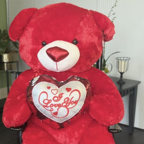 Large red teddy bear holding a heart pillow that says I Love You