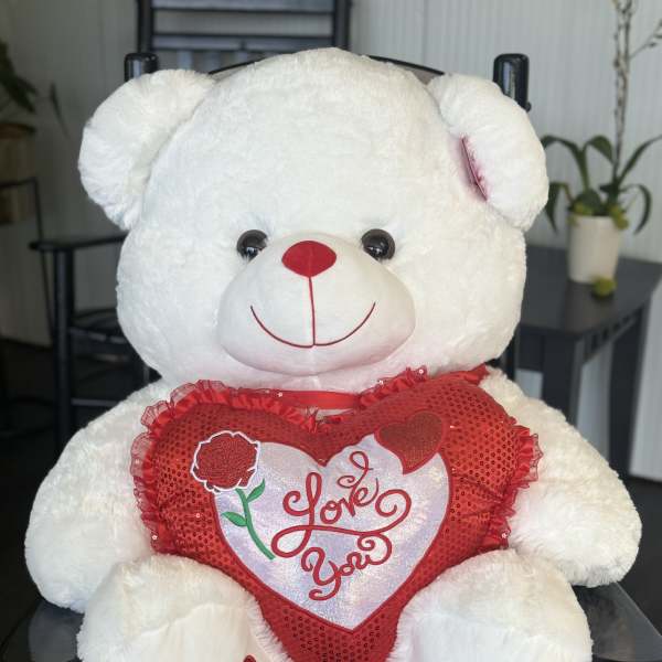 White teddy bear holding a red heart pillow with "Love You" text