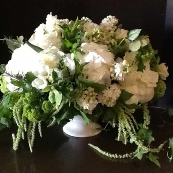 White floral arrangement in a low white vase with trailing greenery
