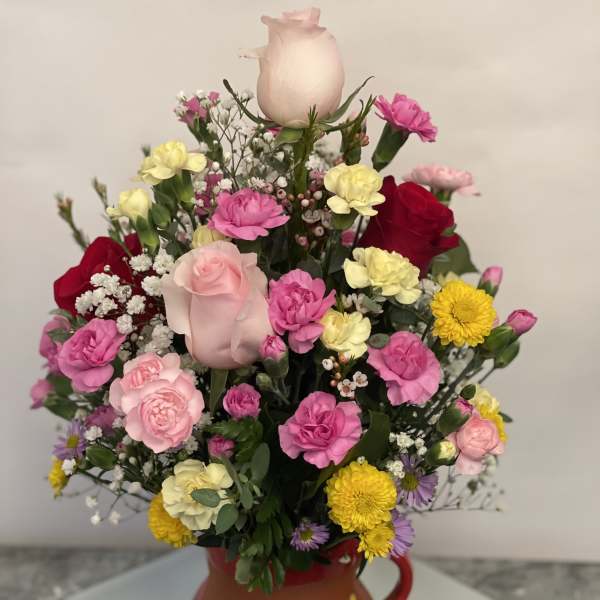 Mixed bouquet in a painted ceramic pitcher with pink, yellow, and red blooms
