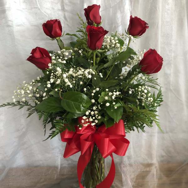 Red roses in a glass vase with baby's breath and a red ribbon