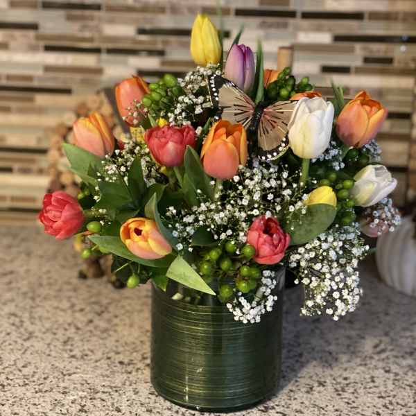 Colorful tulips arranged in a green vase with a butterfly accent