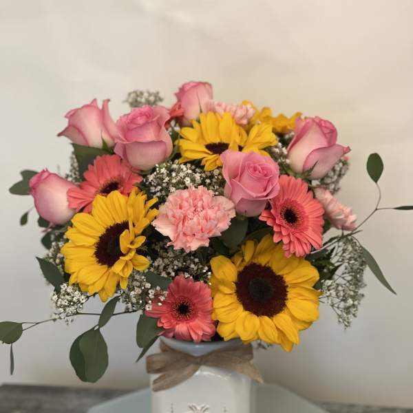 Pink roses and gerbera daisies with yellow sunflowers in a white vase
