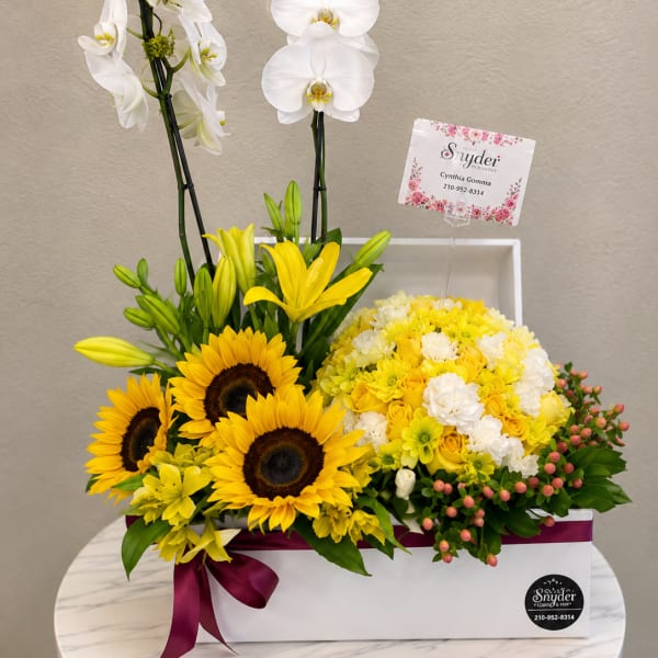 Yellow and white floral arrangement with orchids, sunflowers, and roses in a white box