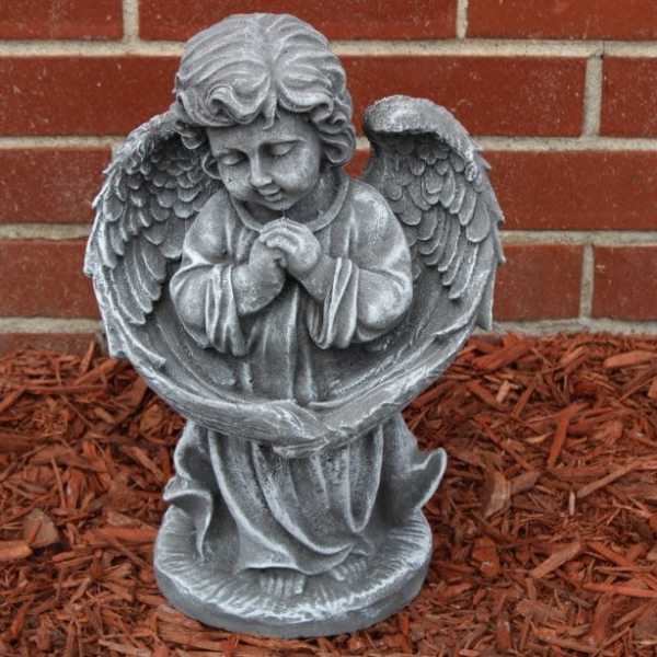 Gray angel statue with folded hands in front of a brick wall