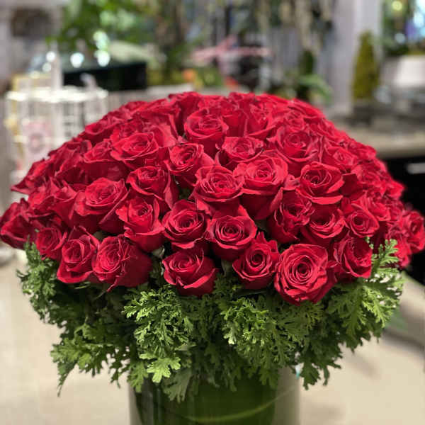 Large dome of red roses with a green foliage collar in a clear glass cylinder vase.