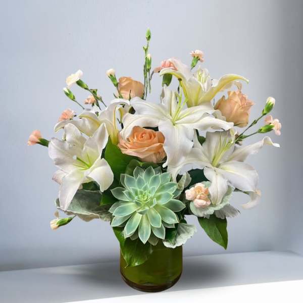 White lilies and peach roses in a green glass vase with a succulent accent