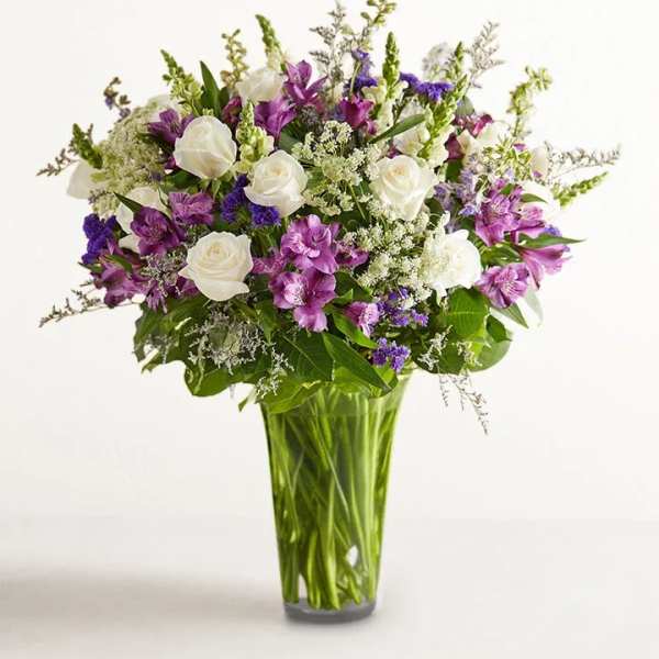 Bouquet of white roses and purple flowers in a tall glass vase