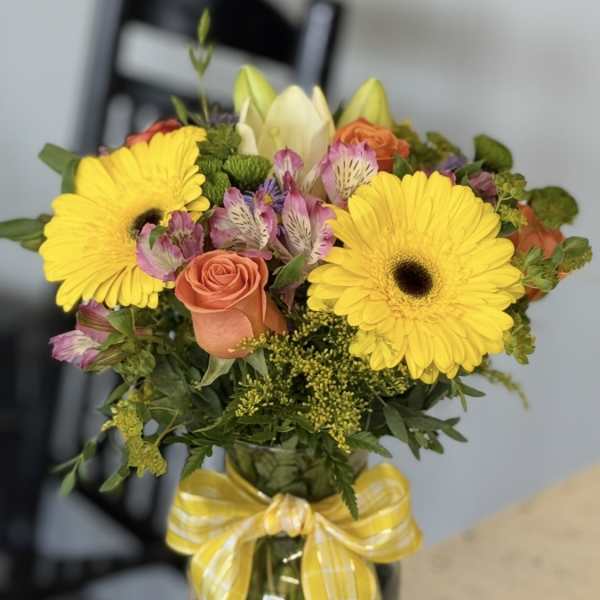 Bouquet of yellow gerbera daisies and peach roses in a glass vase with a yellow ribbon