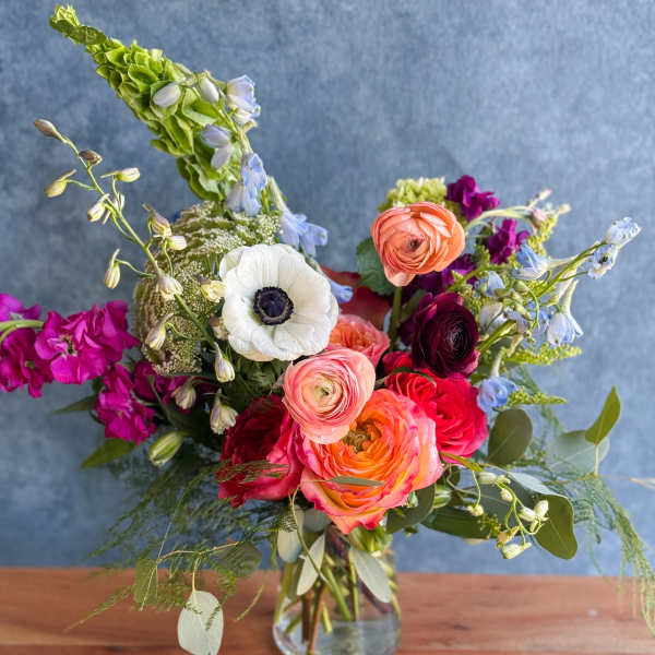 Mixed bouquet in a clear glass vase with pink, orange, white, and blue blooms