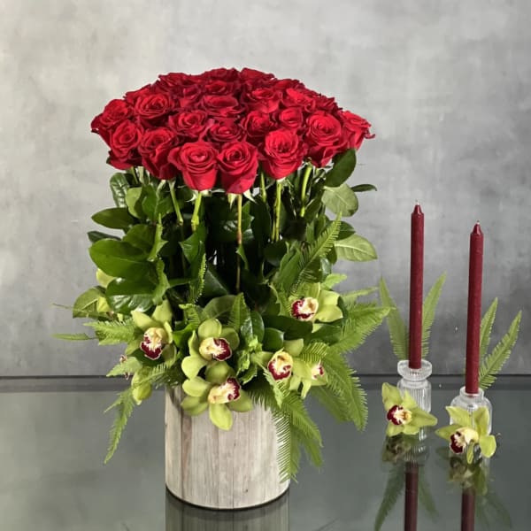 Red rose arrangement in a wooden container with green orchids and ferns