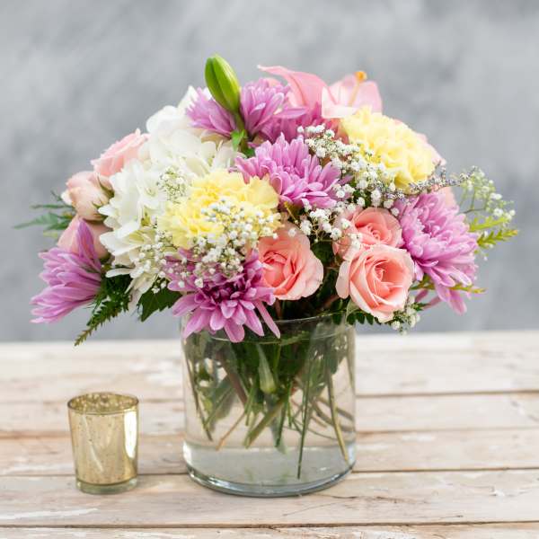 Mixed pink, white, and yellow flowers in a glass vase beside a gold votive