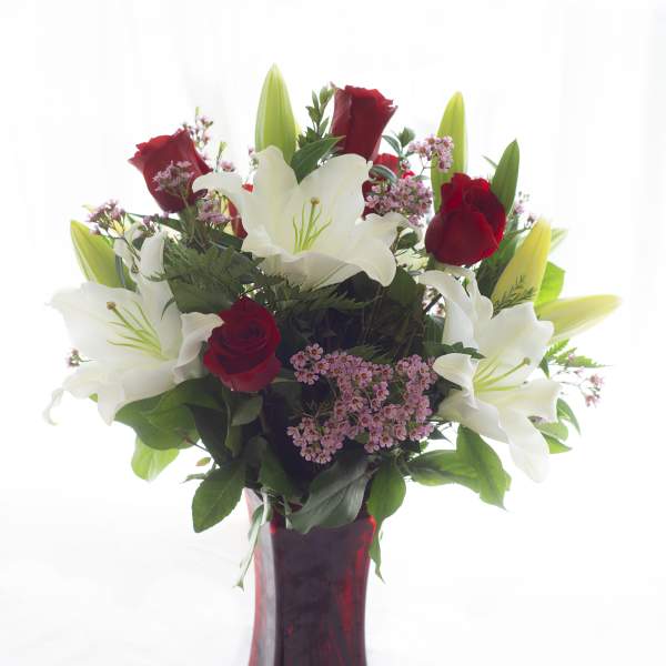 Red roses and white lilies arranged in a red glass vase