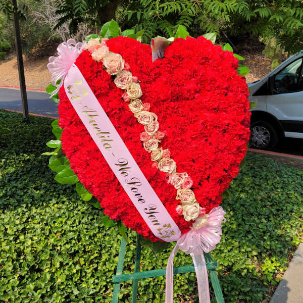 Heart-shaped red floral standing spray with a pink ribbon and pale roses