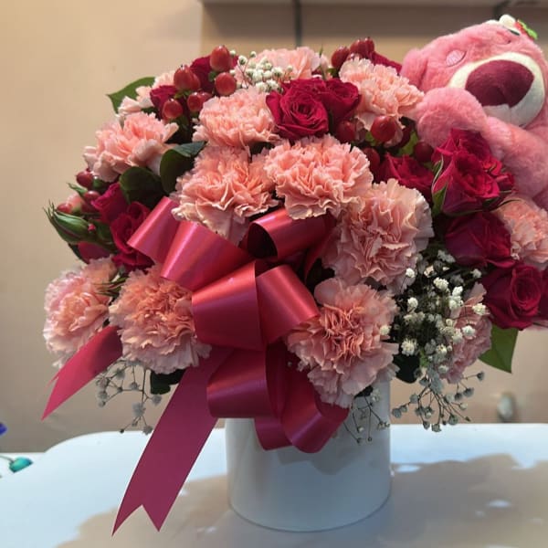 Pink and red bouquet with carnations, roses, and a teddy bear in a white box