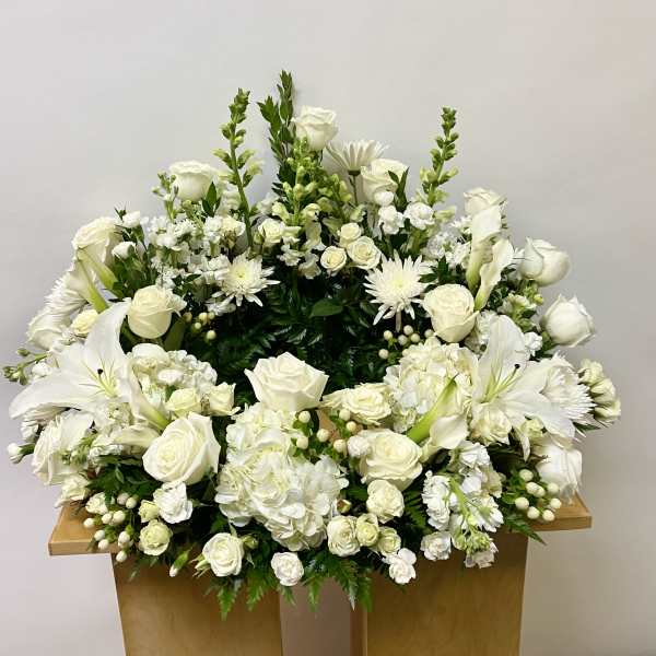 Large white floral arrangement with roses, lilies, and hydrangeas on a wooden stand