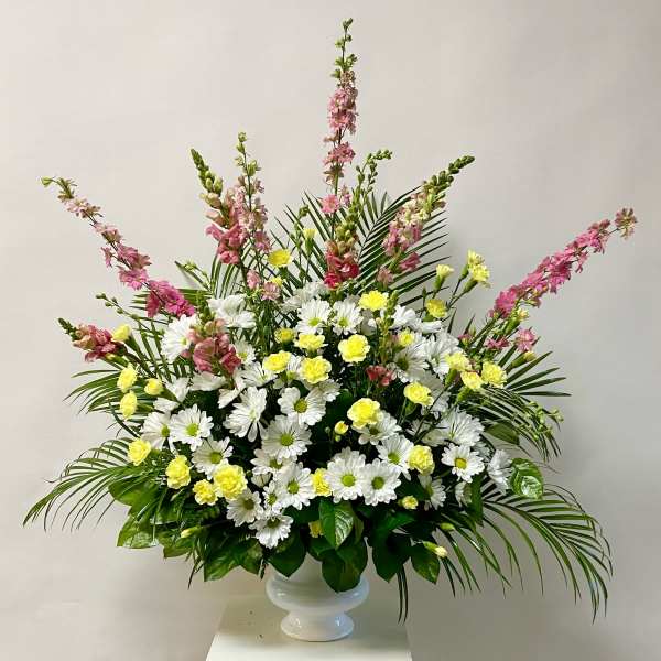 White daisies and yellow carnations in a white pedestal vase