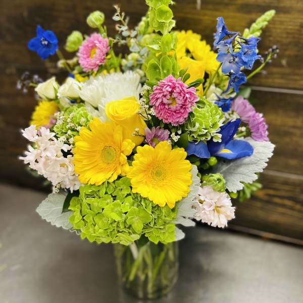 Colorful mixed bouquet in a clear glass vase with yellow, blue, pink, and white blooms