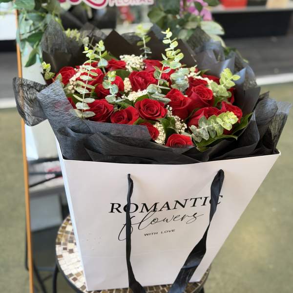 Bouquet of red roses with eucalyptus in a white gift bag