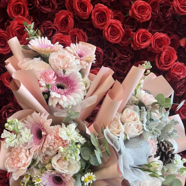Two pastel bouquets with roses, gerbera daisies, and carnations against a red rose wall