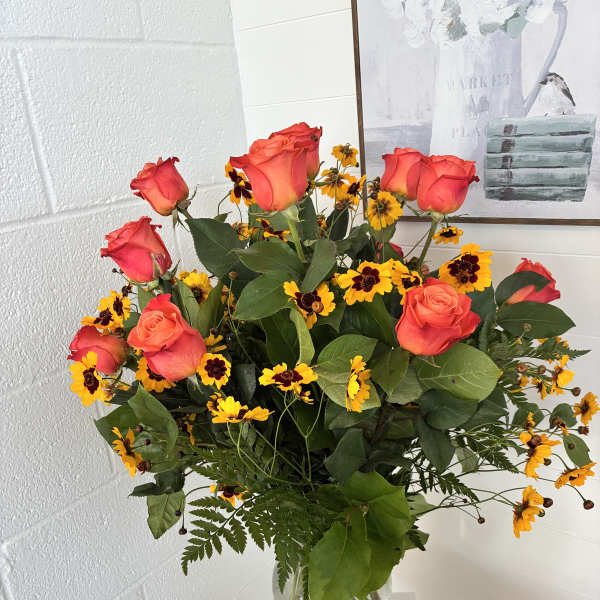 Bouquet of coral roses and yellow daisies in a clear glass vase