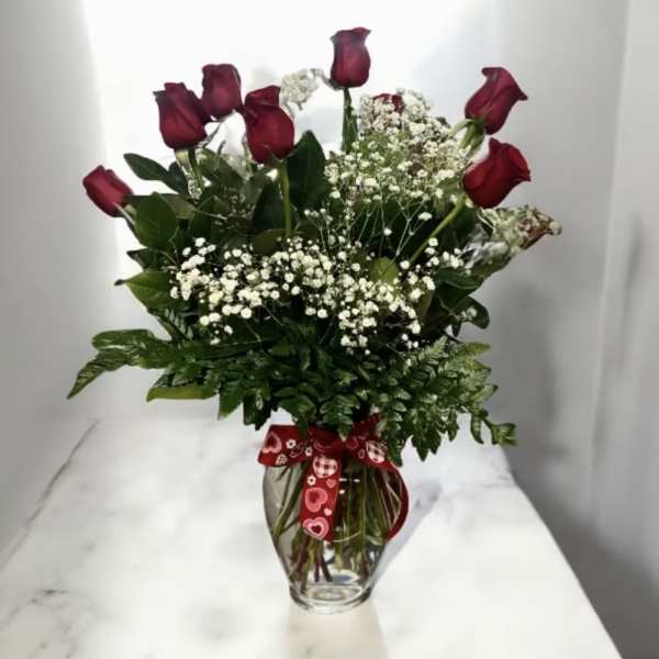 Red roses with baby's breath in a glass vase with a heart ribbon