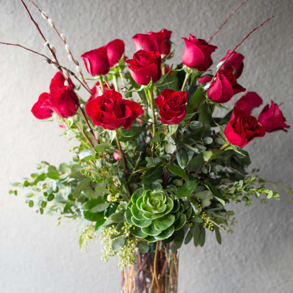 Red roses arranged in a clear glass vase with greenery and a succulent accent