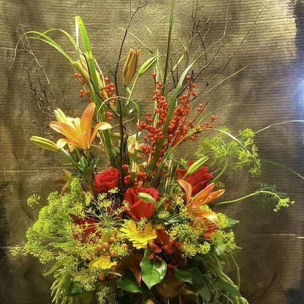 Tall floral arrangement with red roses, orange lilies, and red berry stems