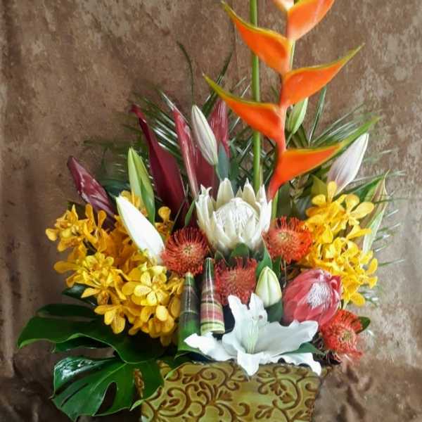 Tropical floral arrangement with orange heliconia and white lilies in a decorative container