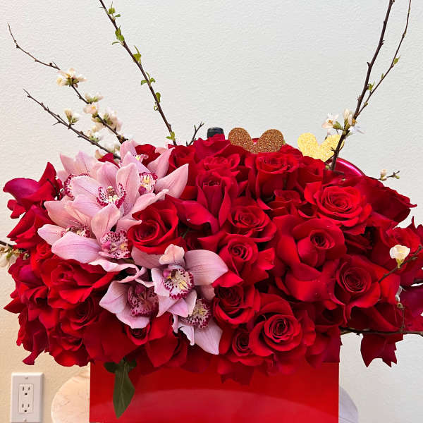 Red roses with pink orchids in a red box, accented by flowering branches.