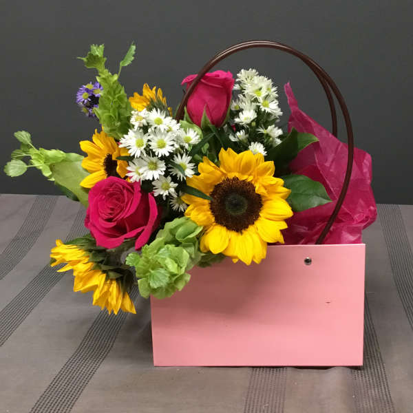 Pink gift bag with sunflowers, roses, and white daisies