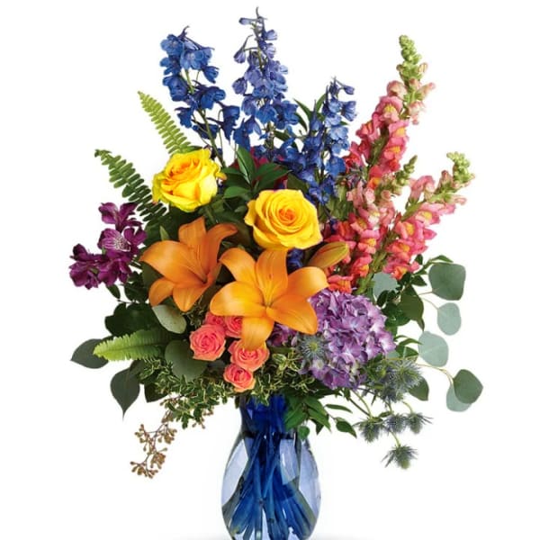 Colorful bouquet with roses, lilies, delphinium, and snapdragons in a blue glass vase