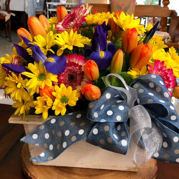 Mixed bouquet of yellow daisies, orange tulips, and purple irises with a polka-dot ribbon